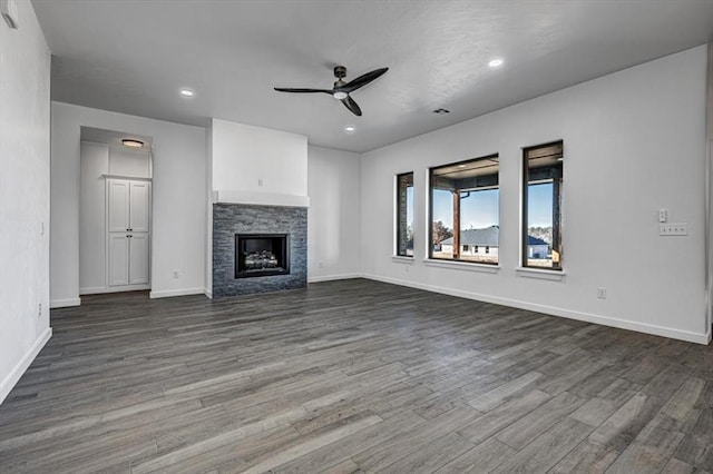 unfurnished living room featuring a stone fireplace, ceiling fan, and dark hardwood / wood-style flooring