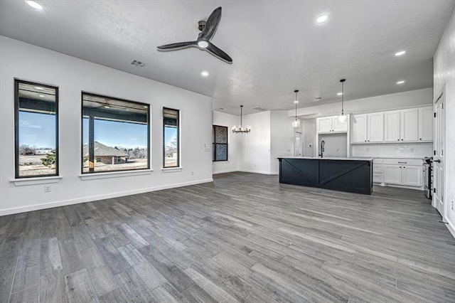 kitchen with an island with sink, white cabinetry, wood-type flooring, and decorative light fixtures