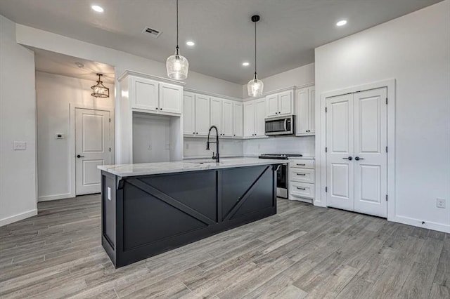 kitchen featuring decorative light fixtures, white cabinets, a kitchen island with sink, and appliances with stainless steel finishes