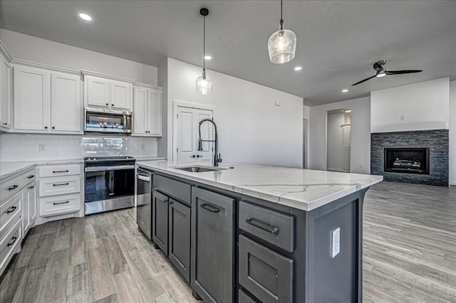 kitchen with appliances with stainless steel finishes, white cabinetry, tasteful backsplash, sink, and a kitchen island with sink