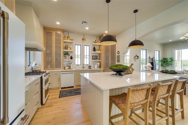 kitchen featuring hanging light fixtures, a spacious island, white appliances, a breakfast bar, and light hardwood / wood-style floors