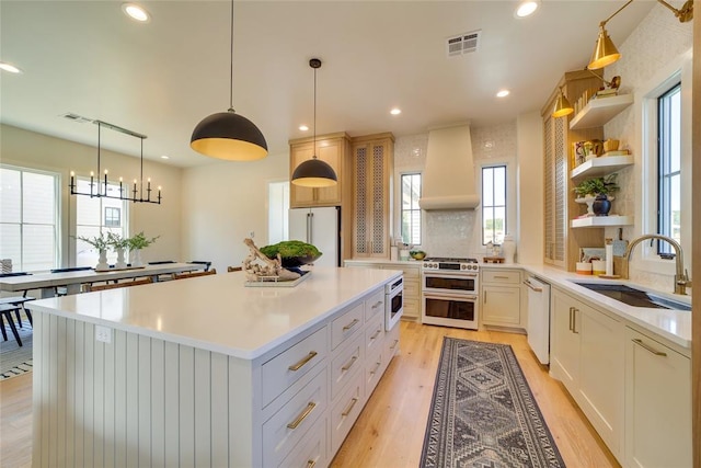 kitchen with white appliances, white cabinets, a center island, custom exhaust hood, and sink