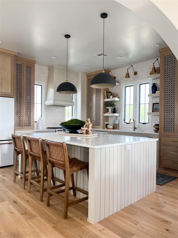 kitchen featuring custom exhaust hood, a large island, decorative light fixtures, light hardwood / wood-style flooring, and white refrigerator