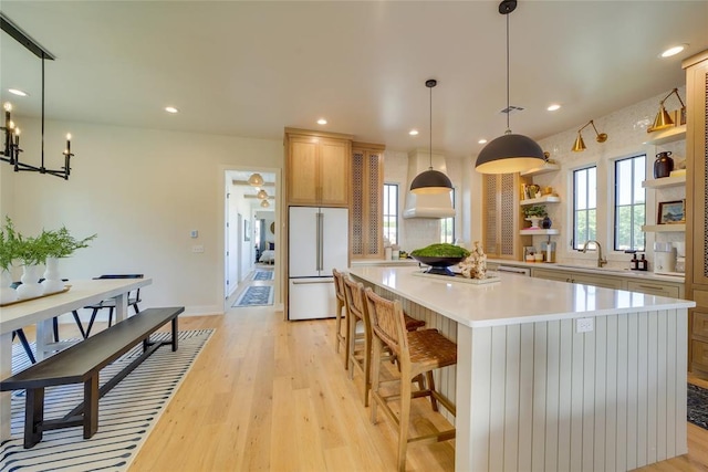 kitchen featuring pendant lighting, a large island, high end white fridge, sink, and light wood-type flooring