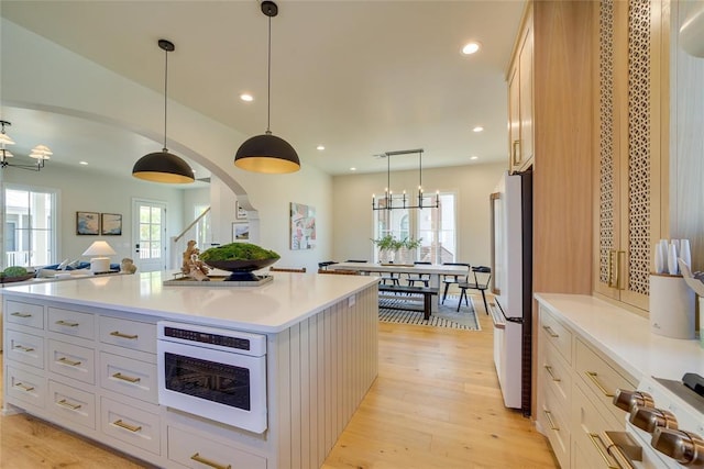 kitchen with white appliances, light hardwood / wood-style floors, white cabinets, a kitchen island, and pendant lighting