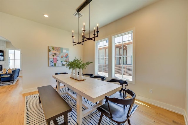 dining room featuring a large fireplace, light wood-type flooring, and a notable chandelier