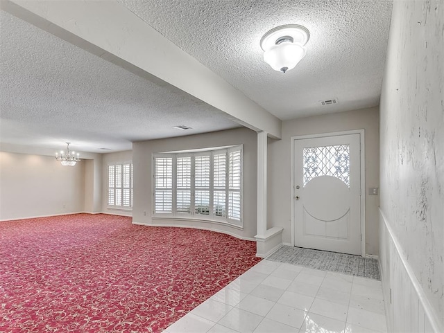 tiled entryway with a healthy amount of sunlight, a notable chandelier, and a textured ceiling