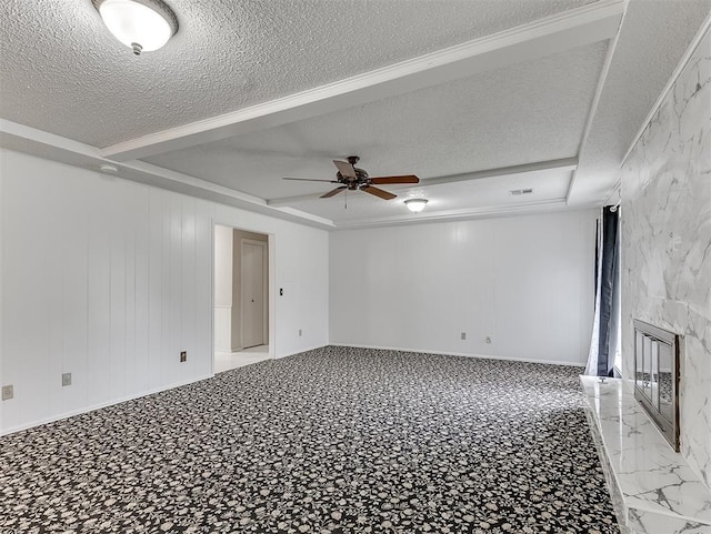 spare room featuring ceiling fan, a fireplace, a raised ceiling, and a textured ceiling