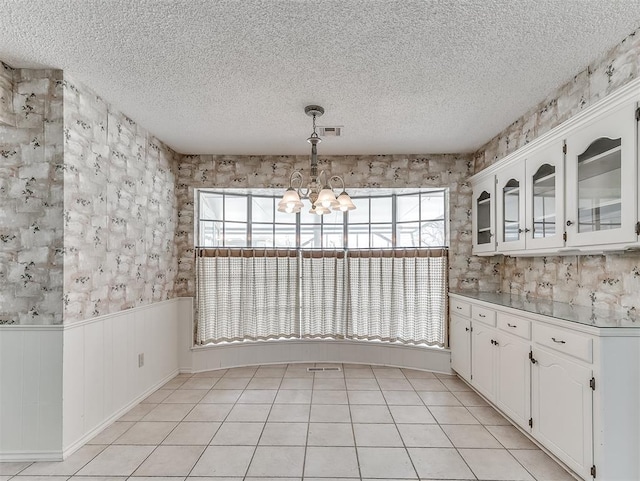 unfurnished dining area with a notable chandelier, light tile patterned floors, and a textured ceiling