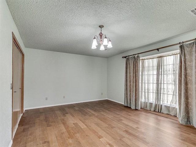 empty room featuring a textured ceiling, a chandelier, and light wood-type flooring