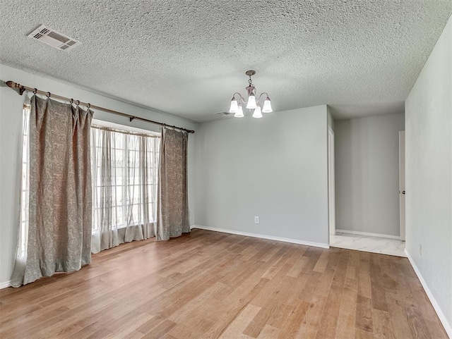 spare room featuring a notable chandelier, a textured ceiling, and light hardwood / wood-style flooring