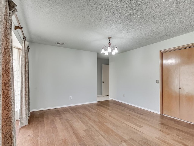 spare room featuring a notable chandelier, a textured ceiling, and light hardwood / wood-style flooring