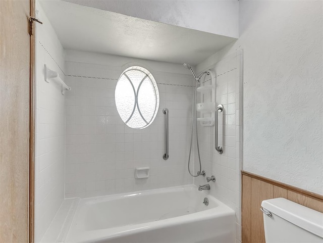 bathroom featuring tiled shower / bath, toilet, and wood walls