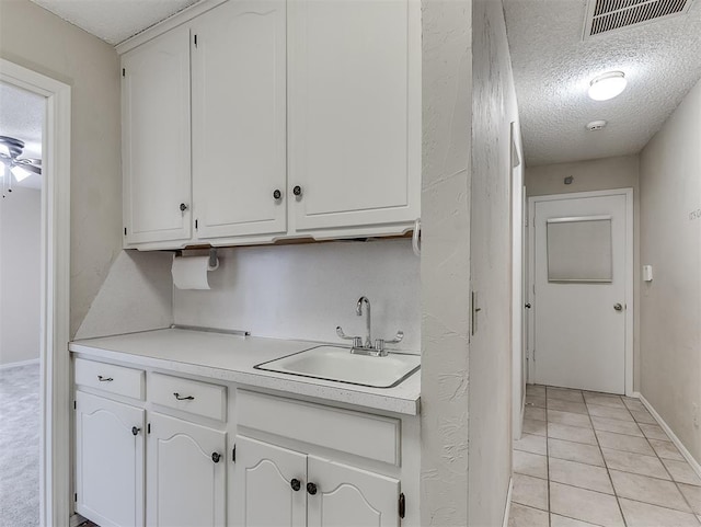 kitchen with white cabinetry, sink, light tile patterned flooring, and a textured ceiling