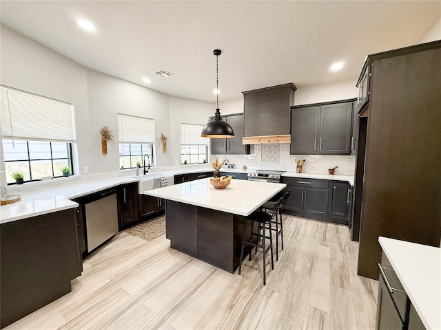 kitchen featuring appliances with stainless steel finishes, decorative light fixtures, premium range hood, backsplash, and a breakfast bar