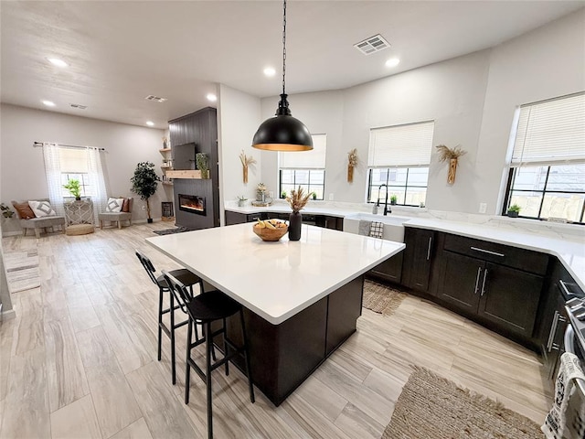 kitchen featuring a spacious island, light wood-type flooring, decorative light fixtures, a large fireplace, and a breakfast bar