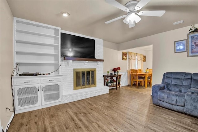 living room with ceiling fan, hardwood / wood-style floors, and a brick fireplace