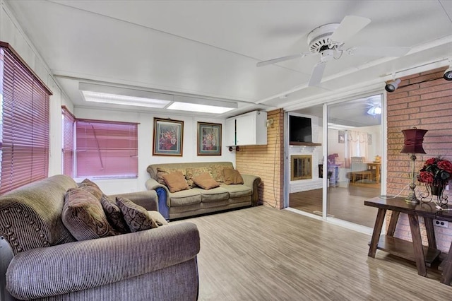 living room featuring light wood-type flooring, ceiling fan, and a brick fireplace