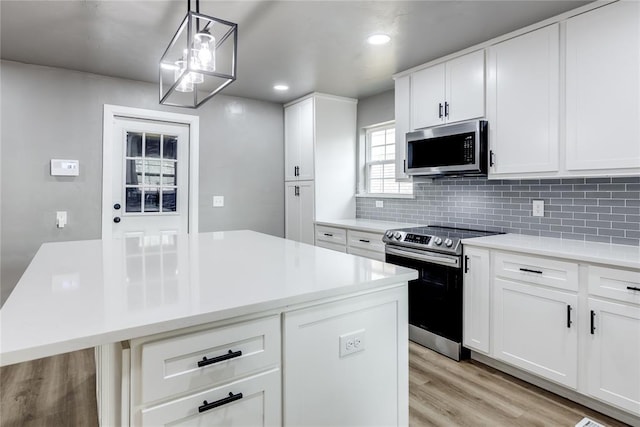 kitchen featuring white cabinets, appliances with stainless steel finishes, a kitchen island, decorative light fixtures, and tasteful backsplash