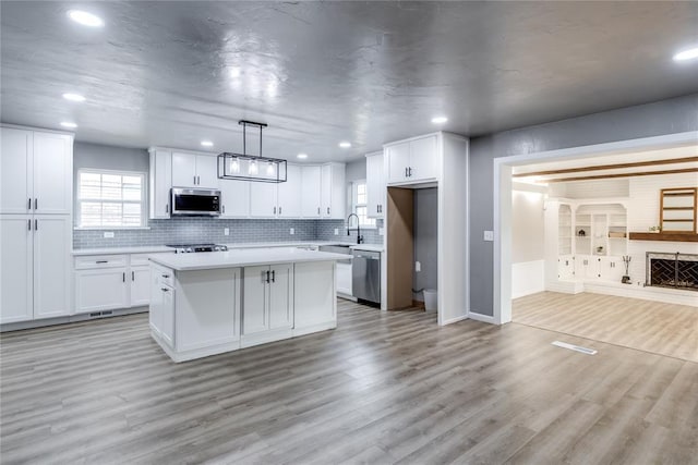 kitchen featuring decorative light fixtures, white cabinets, stainless steel appliances, and a kitchen island