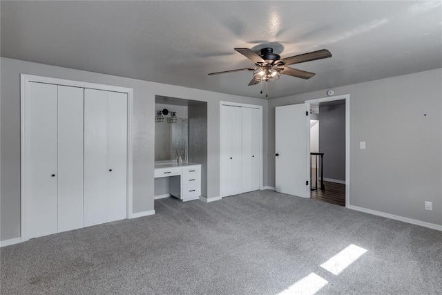 unfurnished bedroom with multiple closets, ceiling fan, ensuite bathroom, carpet, and built in desk