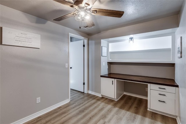 unfurnished office featuring built in desk, ceiling fan, light hardwood / wood-style flooring, and a textured ceiling