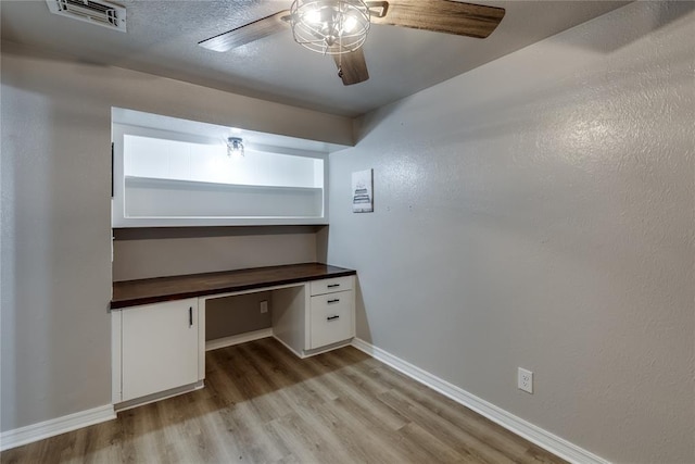 unfurnished office with ceiling fan, built in desk, and light wood-type flooring