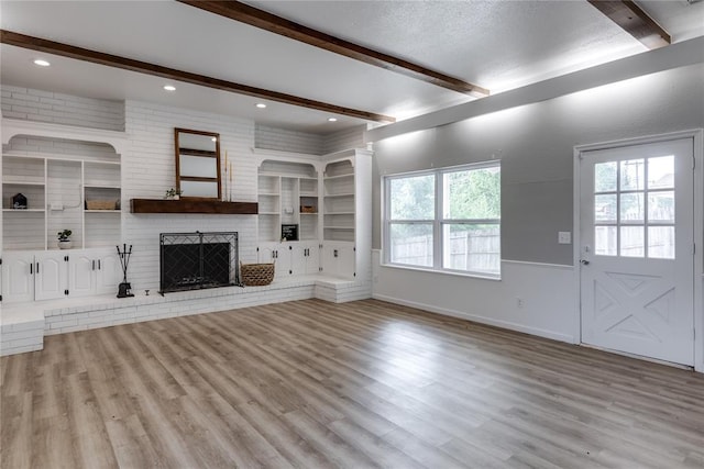 unfurnished living room featuring a textured ceiling, light hardwood / wood-style flooring, beam ceiling, and a brick fireplace