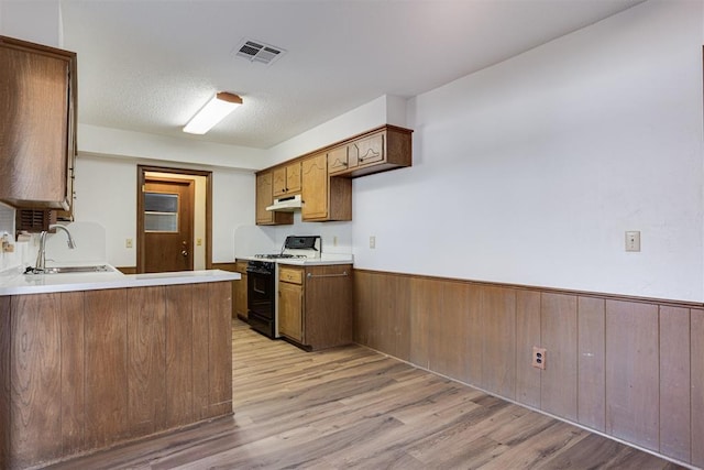 kitchen with light wood-style floors, gas stove, a wainscoted wall, and under cabinet range hood