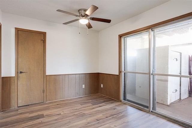 empty room with a ceiling fan, wood finished floors, a wainscoted wall, and wood walls