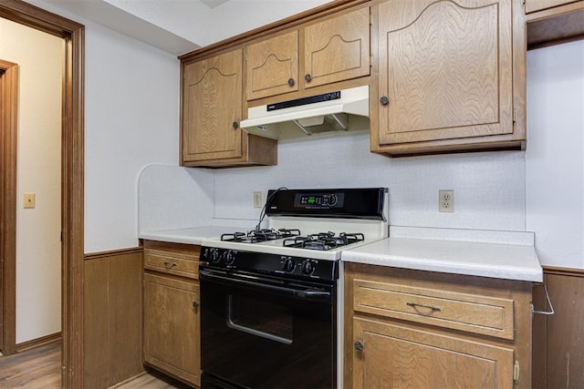 kitchen with range with gas stovetop, light countertops, under cabinet range hood, and wainscoting