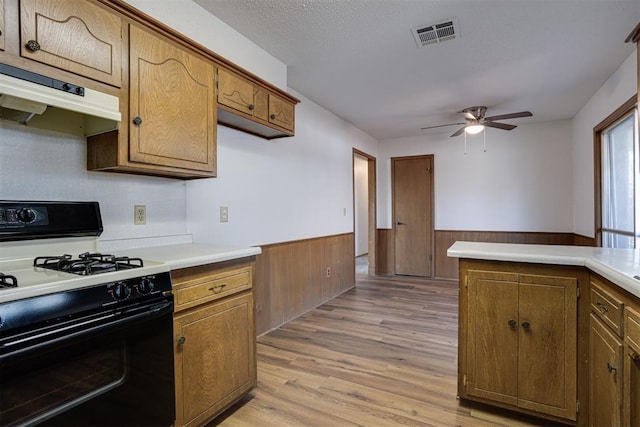 kitchen featuring a wainscoted wall, visible vents, under cabinet range hood, black gas range oven, and ceiling fan