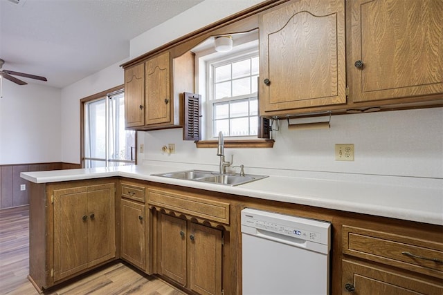 kitchen featuring a wainscoted wall, a peninsula, white dishwasher, ceiling fan, and a sink