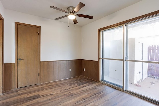 empty room featuring a wainscoted wall, wood finished floors, a ceiling fan, and wood walls