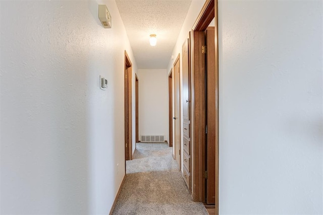 corridor with visible vents, light colored carpet, a textured ceiling, and a textured wall