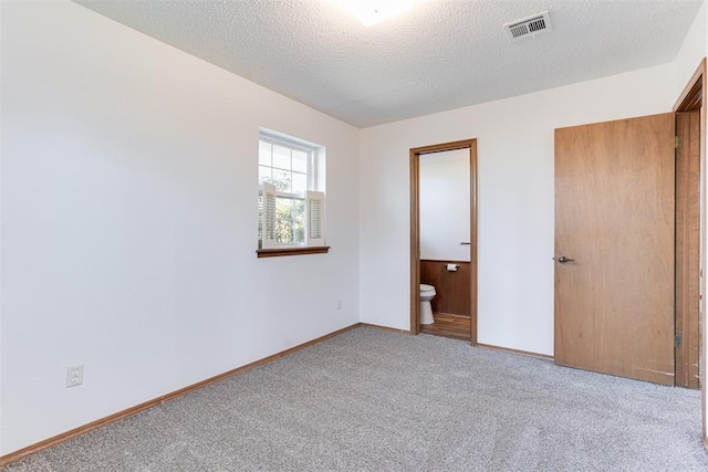 unfurnished bedroom featuring visible vents, a textured ceiling, connected bathroom, carpet floors, and baseboards