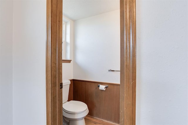 bathroom featuring toilet, wood finished floors, wood walls, and wainscoting