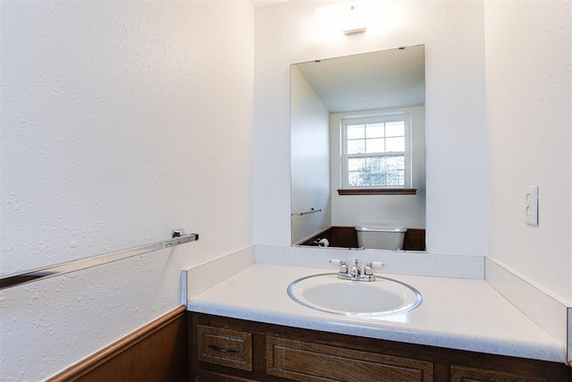 half bath featuring a wainscoted wall, toilet, and vanity