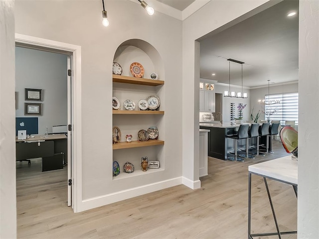 hall featuring crown molding, an inviting chandelier, built in features, and light hardwood / wood-style flooring