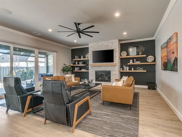 living room featuring ornamental molding, a stone fireplace, ceiling fan, and light hardwood / wood-style floors