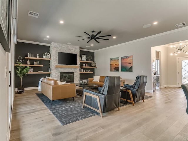 living room featuring crown molding, a stone fireplace, ceiling fan with notable chandelier, and light hardwood / wood-style floors