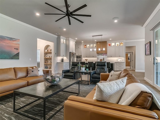 living room with built in shelves, wood-type flooring, ornamental molding, and ceiling fan