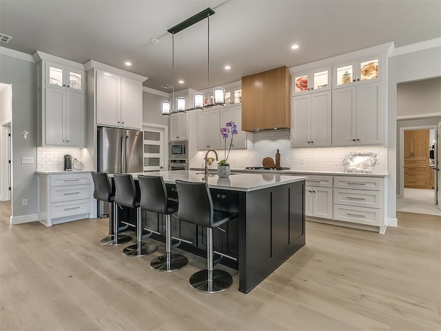 kitchen with appliances with stainless steel finishes, a kitchen island with sink, white cabinets, and light hardwood / wood-style flooring