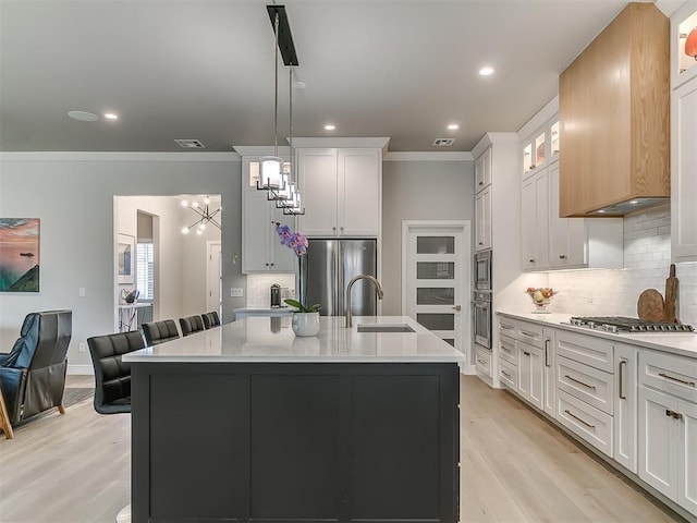 kitchen featuring premium range hood, appliances with stainless steel finishes, white cabinets, a center island with sink, and decorative light fixtures