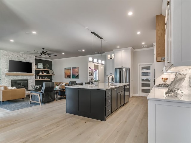 kitchen featuring sink, a kitchen island with sink, hanging light fixtures, ornamental molding, and white cabinets