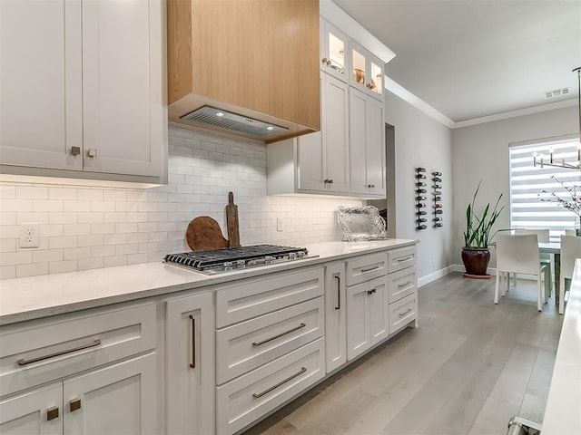 kitchen featuring tasteful backsplash, white cabinetry, hanging light fixtures, stainless steel gas cooktop, and crown molding