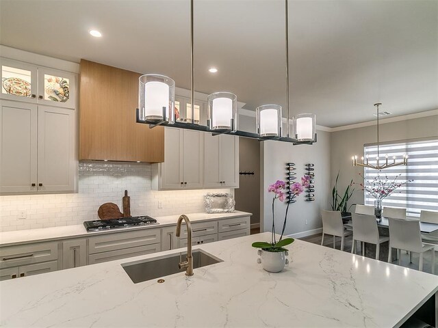 kitchen featuring sink, backsplash, light stone counters, decorative light fixtures, and stainless steel gas stovetop