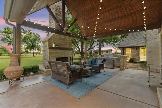 patio terrace at dusk featuring exterior kitchen, a lawn, grilling area, and an outdoor living space with a fireplace