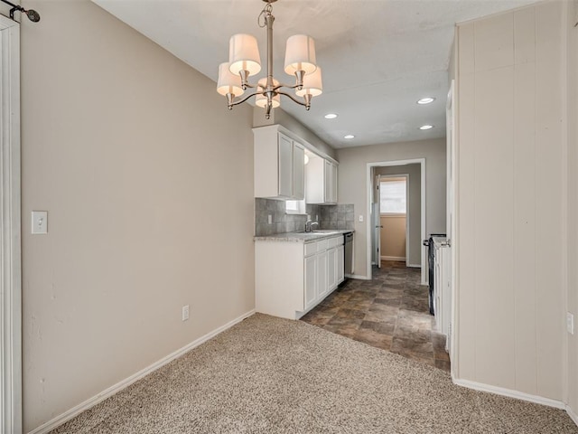 kitchen with pendant lighting, white cabinetry, sink, dark colored carpet, and a notable chandelier