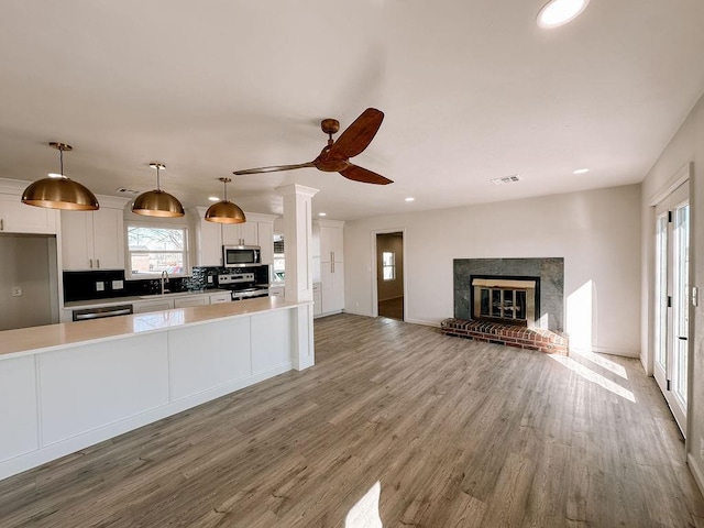 kitchen with wood-type flooring, pendant lighting, white cabinets, decorative backsplash, and stainless steel appliances